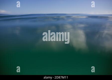 Clouds reflected on the surface of a calm turquoise ocean in Hawaii Stock Photo