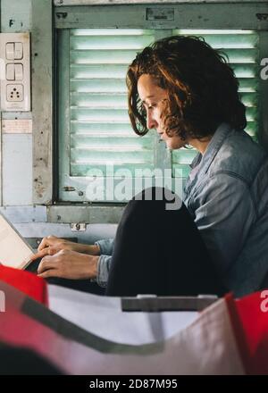 Young european woman working on her tablet while traveling from New Delhi to Agra on a sleeper class train. Stock Photo