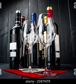 Bright wine glasses on red tablecloth, bottles of red wine on gray wooden background Stock Photo