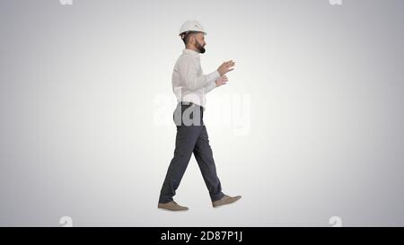 Engineer in hardhat walking and explaining something on gradient Stock Photo