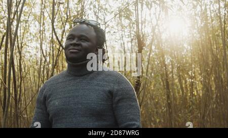 Young african man walkling through the woods looking. Sunrays coming through trees. High quality photo Stock Photo