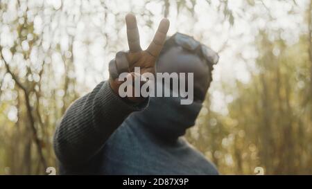 African american man with rolling neck sweater over his nose and mouth shoving peace sign with fngers. High quality photo Stock Photo