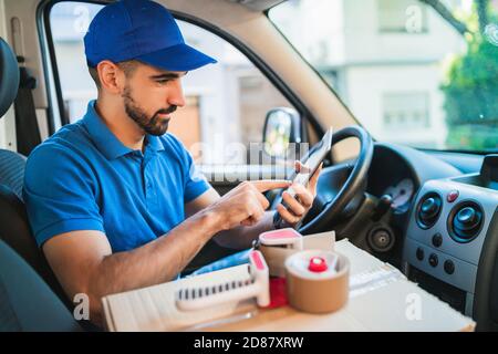 Portrait of a delivery man driver using digital tablet while sitting in van. Delivery service and shipping concept. Stock Photo
