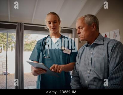 Young female doctor showing medical report to senior patient on digital tablet in hospital Stock Photo