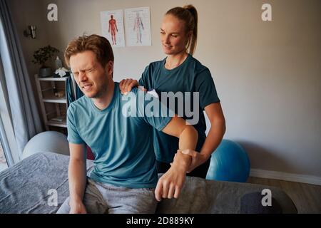 Handsome young male patient suffering from hand injury exercising with female physiotherapist Stock Photo