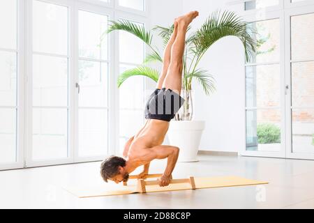 Man doing a handstand push-up using floor bars balancing on his hands while performing a calisthenetic workout in a high key gym in a health and fitne Stock Photo