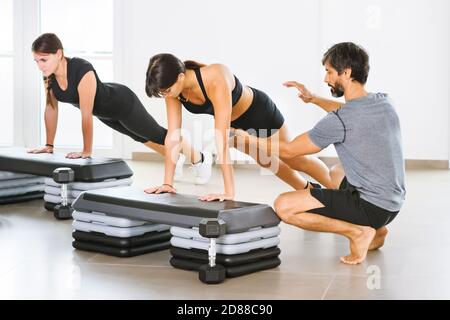 Young male personal trainer assisting a woman doing a yoga plank pose in a class in a bright airy gym in a health and fitness or healthy lifestyle con Stock Photo