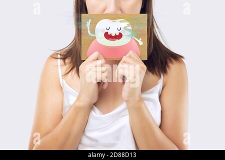 A woman wearing a white dress holding a white paper with an open mouth cartoon image. On a light gray background. Bad breath or Halitosis. The concept Stock Photo