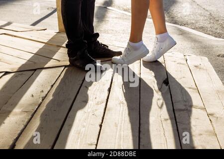 Womens legs in white sneakers are on their toes. Male feet are standing nearby Stock Photo