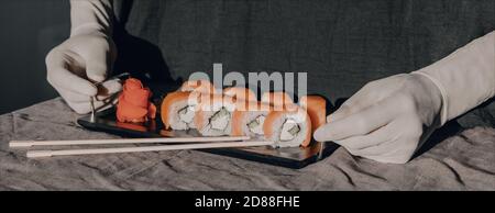 Hands in rubber gloves serve sushi on a black stand. Sushi menu. Stock Photo