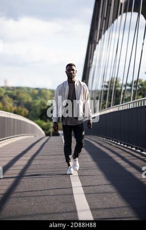 Confident young black man walking towards camera with confidence. Full length. Vertical. Stock Photo