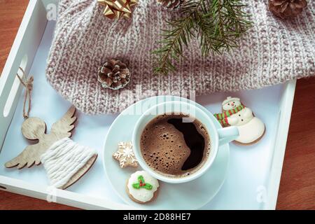 A cup of coffee on a tray with gingerbread, a spruce branch, toy angel and a knitted sweater. Christmas layout, top view. Stock Photo