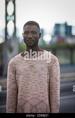 Handsome black man posing in sweater standing outdoors. Medium shot. Focus on foreground. Front view. Stock Photo