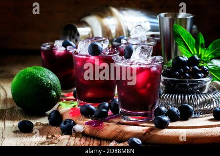 Alcoholic cocktail Darkside, with liqueur, blueberry, lime juice, crushed ice, bar tools on a vintage wooden background, selective focus Stock Photo
