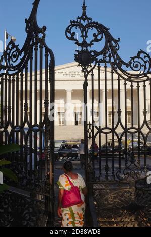 A woman passes through a wrought iron gate of Horniman Circle Garden; b/g: former Bombay Town Hall housing the Asiactic Society; Fort, Mumbai, India Stock Photo