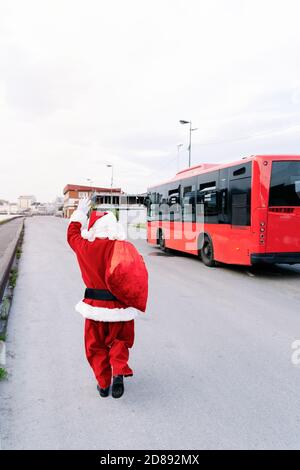 Back portrait of Santa Claus running around worried and calling a bus because he's lost it and has to deliver the presents to the kids in Christmas 20 Stock Photo
