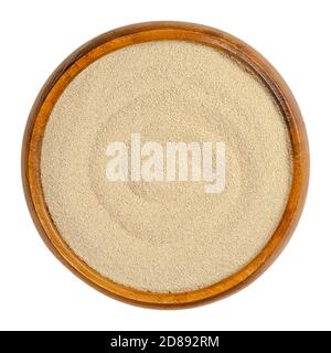 Dry yeast in a wooden bowl. Small oblong granules of active bakers yeast, commonly used in baking bread and bakery products. Close-up, from above. Stock Photo