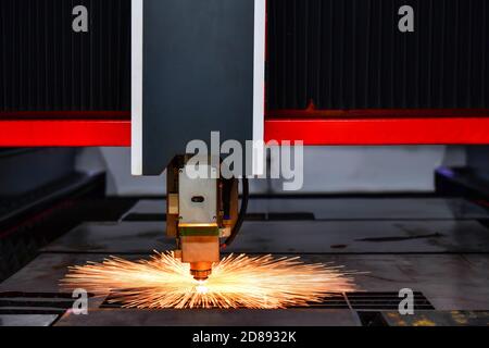 Close up laser cut head machine while cutting the sheet metal with the sparking light in factory Stock Photo