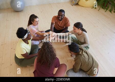 Multiethnic group of people sitting on the floor in circle and holding hands during classes Stock Photo