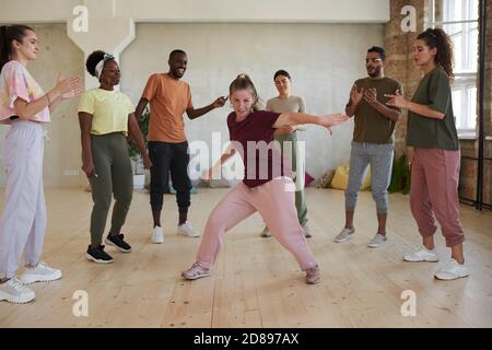Young woman showing dance exercises while other people standing in circle clapping and watching in dance studio Stock Photo