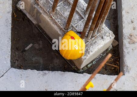 Yellow hard hat, closeup overhead view, on construction building site beside concrete and steel structure. Protective helmet worn by laborers Stock Photo