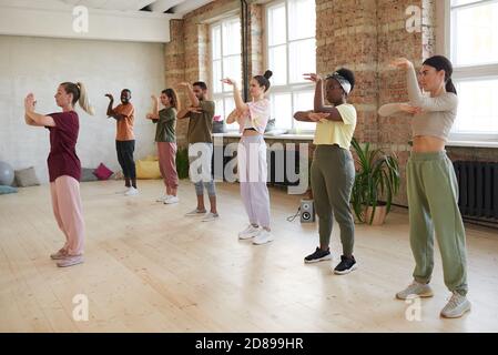 Group of young people standing and repeating the movements of the instructor in exercise class Stock Photo
