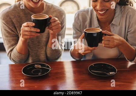 Close-up of two women sitting at cafe table drinking coffee. Female friends having coffee at a coffee shop. Stock Photo