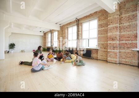 Group of young dancers sitting on the floor resting and talking in dance studio Stock Photo
