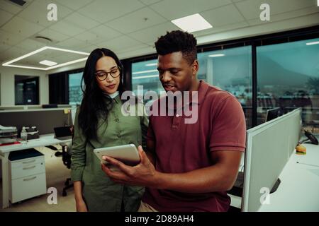 Multi-ethnic partners submitting business report using digital tablet standing in office block Stock Photo