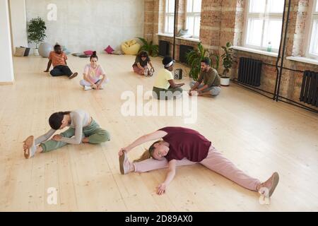 Group of healthy people sitting on the floor and doing stretching exercises during sports training in health club Stock Photo
