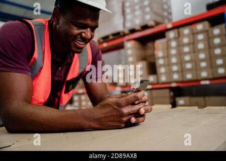 Male worker texting on smartphone chatting to colleagues while standing in warehouse. Stock Photo