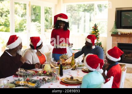 Multigeneration family  wearing santa hats having lunch together while sitting on dining table in the living room at home. christmas festivity traditi Stock Photo