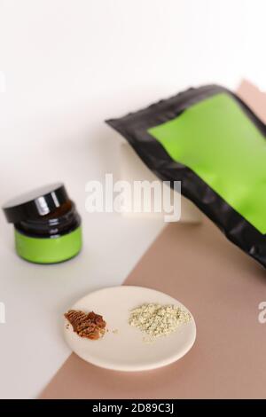 Focus on white plate with clay powder near doypack and jar with cosmetic products and green space for brand. Stock Photo