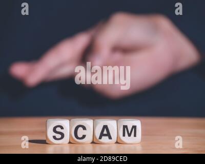 SCAM word made with building wooden blocks on table front of hand of sign language. Business concept and copy space. Stock Photo