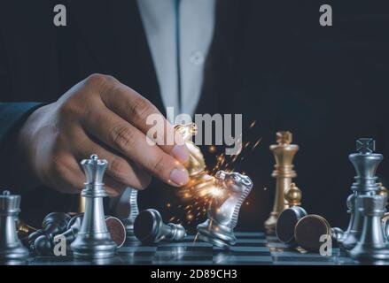 Hand businessman moving the golden knight chess fighting silver knight with fire sparks chess on chess board to successfully in the competition. Manag Stock Photo