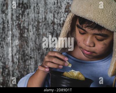 Hungry child eating bread that asking help for food donation from the people on street at the city. Unidentified homeless child begging on street. She Stock Photo