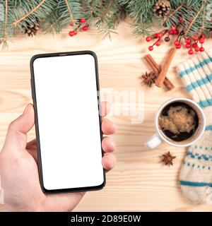 mockup phone on christmas background. Top view of a man holding a phone with blank white screen in hand on wooden New Year or christmas background. Ch Stock Photo