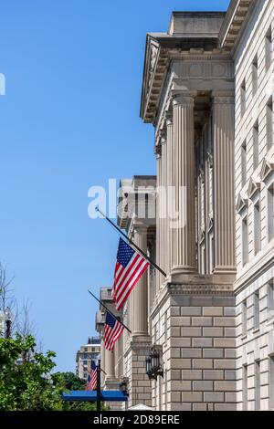 US flags fly at half-staff from the four neoclassical pedimented pavilions of the Herbert C Hoover Building on 15th Street NW, Washington DC Stock Photo