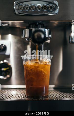 Iced American coffee brewing in plastic cup on coffee machine Stock Photo