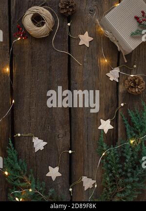 Christmas and New Year's board frame with fir branches, a burning garland, gift box, wooden toys. Rustic wood background, copy space. Stock Photo