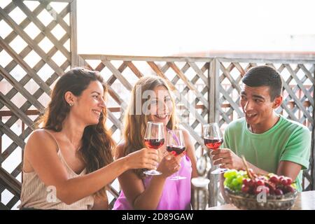 Happy Friends Laughing Loud and Toasting Red Wine Together with White and Red black Grapes on the Table. Balcony Concept with Friends that Spending th Stock Photo