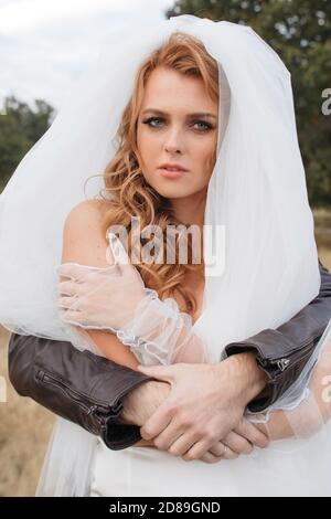 Man in a leather jacked with his arms around a bride Stock Photo
