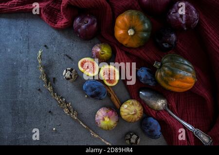 Fresh fruits and vegetables on a table. Top view photo of grapes, pumpkins, plums and figs. Grey textured background. Autumn still life. Stock Photo