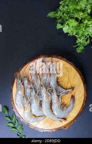 fresh shrimps or white prawns raw on a wooden chopping board with coriander and curry leaves. on background with copy space. Stock Photo