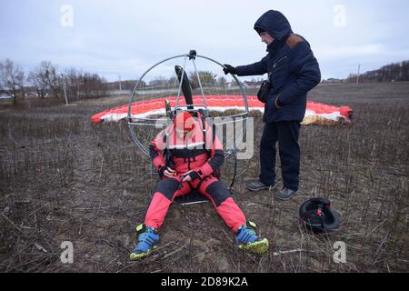 Paramotoring. Instructor starting the engine of paramotor by turning propeller, paramotorist kneeling to help him Stock Photo