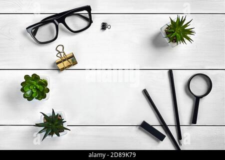White wooden tabletop with black glasses, two pencils, eraser, magnifier, binder clips and three succulents in pots on it. Close up, copy space Stock Photo