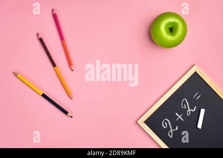 Colorful pencils, green apple and example two plus two written by chalk on small chalkboard, pink background. Close up, copy space Stock Photo