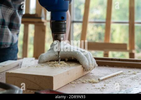 Carpenter working on wood craft at workshop to produce construction material or wooden furniture. The young Asian carpenter use professional tools for Stock Photo