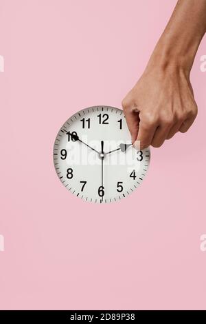 closeup of the hand of a young caucasian man setting a clock backward or forward, at the end or at the beginning of the summer, on a pink background Stock Photo