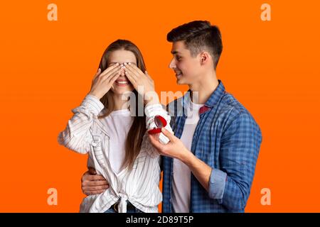 Happy man makes surprise and gives ring in red box, woman covers her eyes with hands Stock Photo